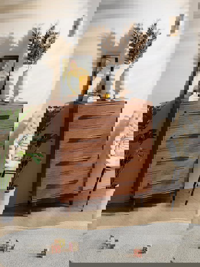 Cómoda de cuatro cajones en madera y pomos horizontales incorporados también de madera. Se ve también una alfombra gris.