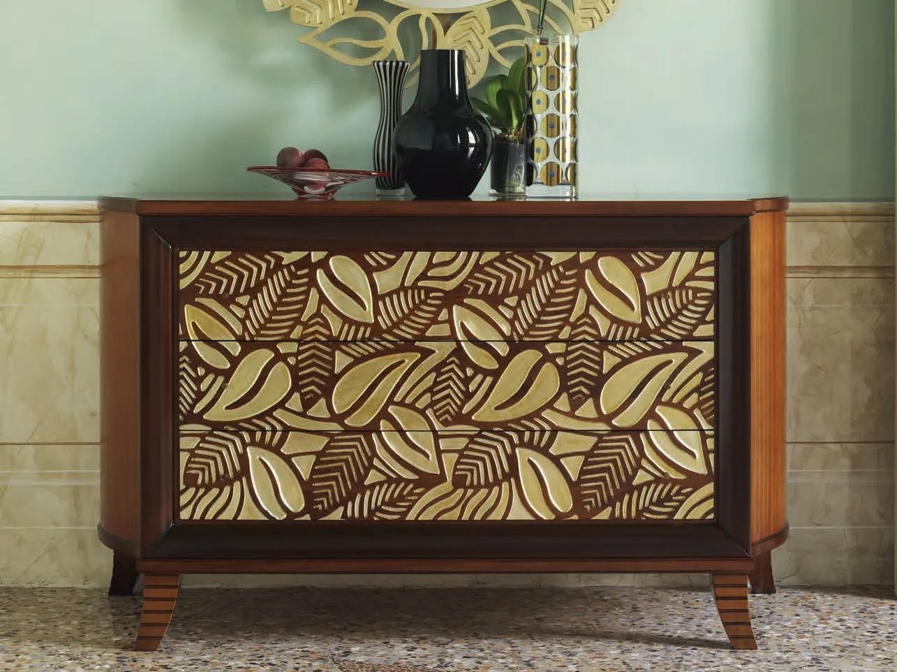 Cómoda de cajones dorados con relieve que dibujan hojas de bordes marrón oscuro. 